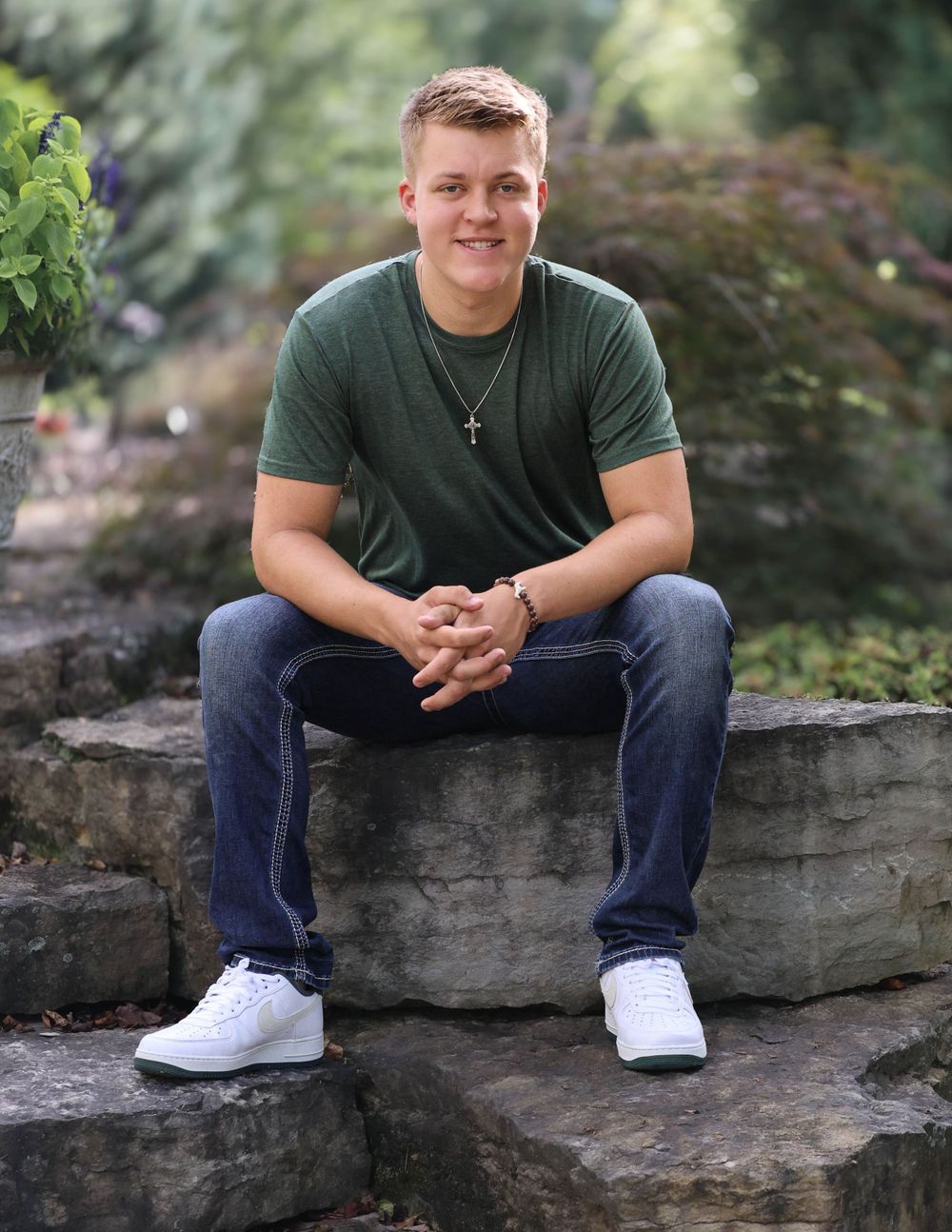 Portrait of someone in green t-shirt sitting on stone wall in garden setting.