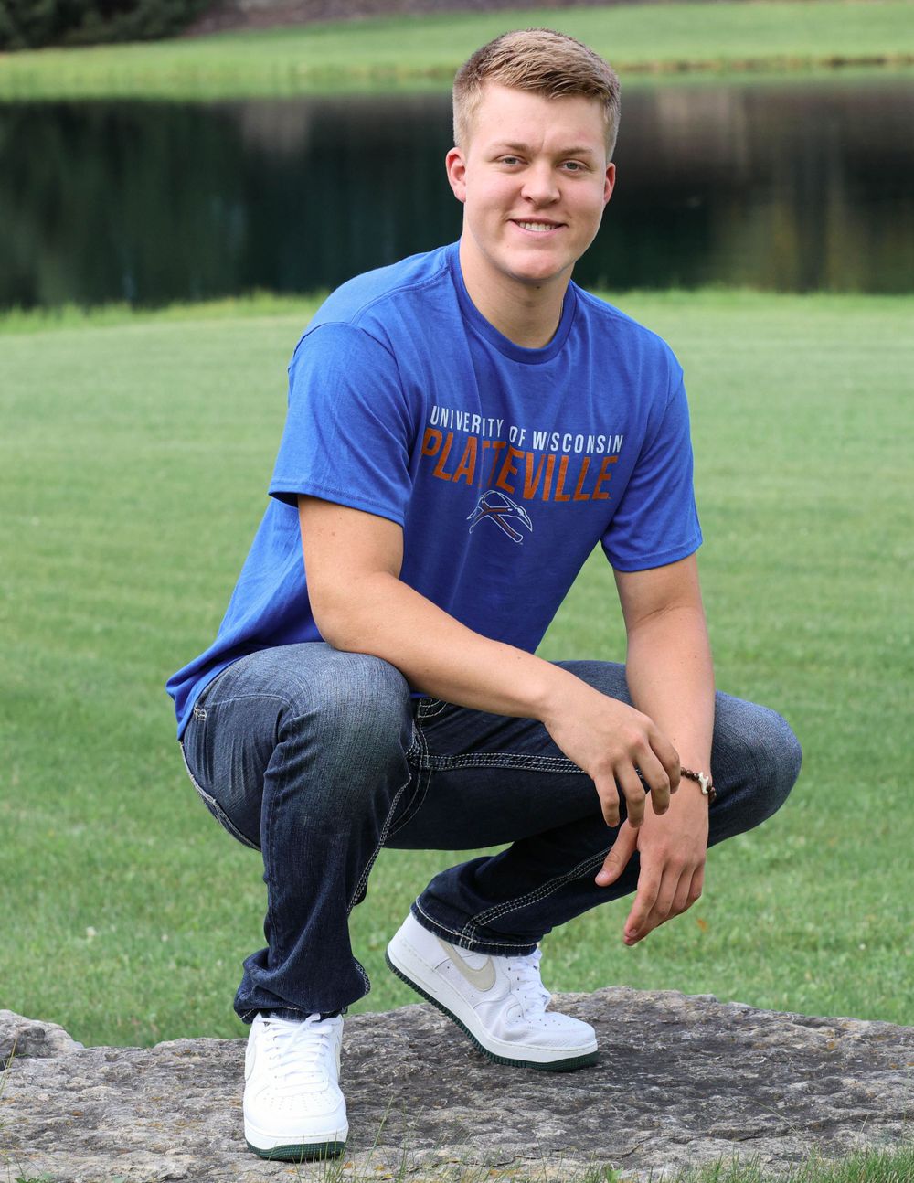 Portrait of someone in blue athletic shirt crouching on rock outdoors.