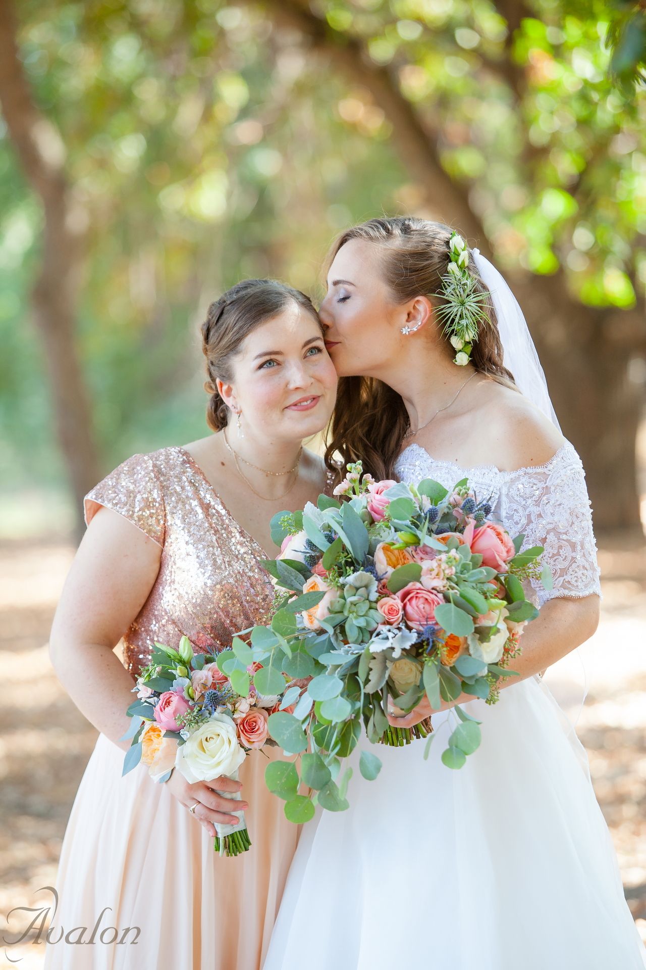 Two people share an intimate moment in wedding attire with a lush bouquet of pink flowers and greenery.