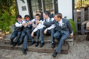 Group of groomsmen in matching grey suits sharing laughs on outdoor steps.