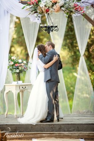 Wedding ceremony setup with white draping, floral arrangements and vintage table under an elegant arch.