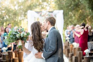 Intimate wedding ceremony moment under white draped arch with wooden bench seating.