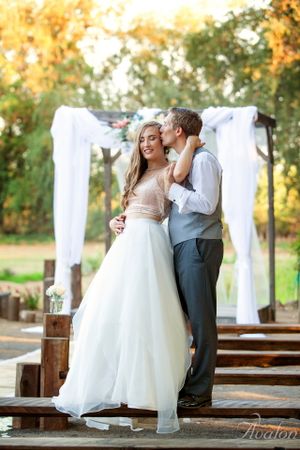 Sweet moment under white draped wedding arch with rustic wooden steps.