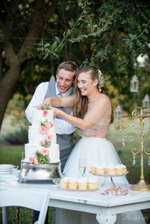Joyful moment cutting an elegant white wedding cake decorated with pink flowers.