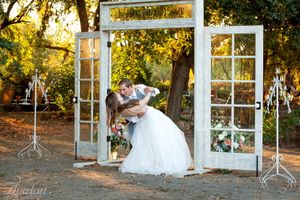 Creative wedding portrait through vintage white window frames in golden outdoor setting.