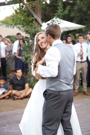 Romantic first dance moment on outdoor dance floor with guests watching in background.