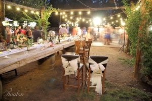 Rustic outdoor wedding reception setup with string lights and decorated wooden chairs.