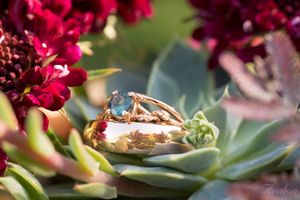 Wedding ring with blue gemstone photographed on succulent with burgundy flowers.
