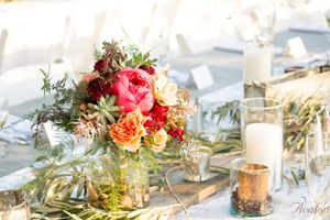 Romantic centerpiece with pink and peach roses, succulents, and candlelight on wedding table.