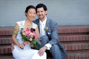 A wedding couple sits together on brick steps with a colorful bouquet.