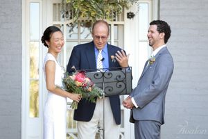 A wedding ceremony takes place on a white porch with an officiant.