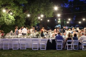 Outdoor wedding reception at night with string lights illuminating long tables and white chairs set up on a lawn.