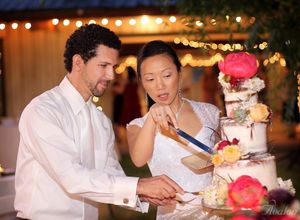 Couple cutting their wedding cake decorated with pink flowers at an evening reception.