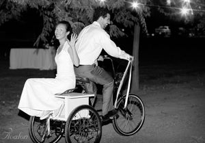 Couple riding together on a vintage bicycle at night under string lights.