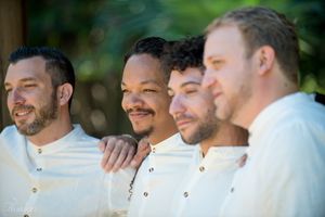 Groomsmen wearing white shirts posing together outdoors.