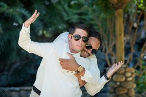 Wedding couple in white attire striking a playful pose outdoors.
