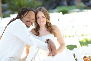 Happy couple in wedding attire sitting together in a sunny outdoor setting.