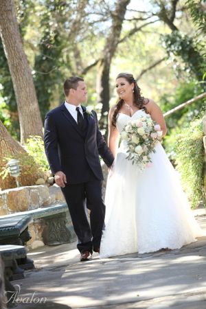 Elegant wedding couple walks along stone-lined garden path during outdoor photo session.