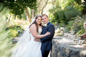 Romantic wedding portrait by stone wall in garden setting with natural lighting.