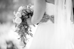 Close-up of cascading bridal bouquet with roses against white wedding dress.