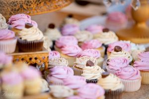 Pink and white frosted cupcakes with floral decorations arranged on a dessert display table.