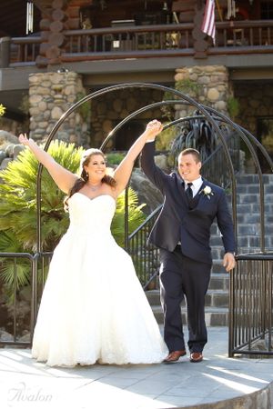 A celebratory moment captured with raised arms under an outdoor arch at a stone venue.