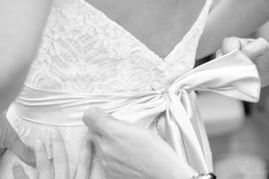 Close-up detail of a white satin bow tied on the back of a lace wedding dress.