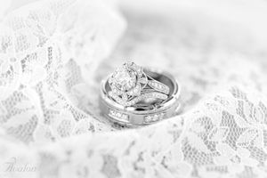 Wedding rings displayed on delicate white lace with diamond engagement ring detail.