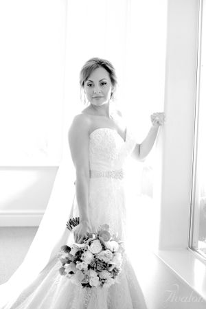 Black and white bridal portrait showing an elegant lace wedding dress beside a bright window.
