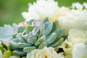 Wedding rings displayed on succulent leaves with white roses in the background.