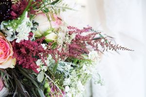 Romantic wedding bouquet featuring pink roses, purple astilbe, and delicate white flowers.