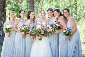 Bridal party in light blue dresses holding pink and white bouquets outdoors.