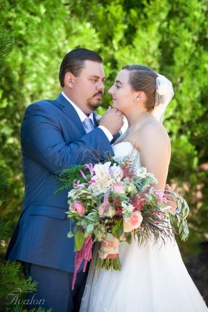 Romantic wedding portrait with couple embracing among green foliage.