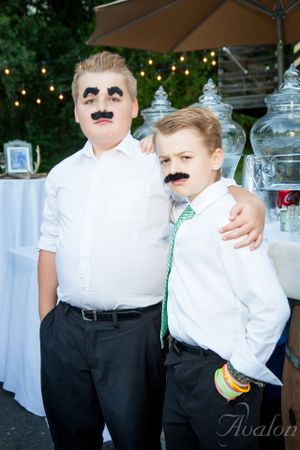 Father and son wearing fake mustaches pose together at wedding reception.