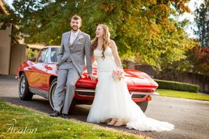 Bride and groom pose together beside classic red Corvette on wedding day.