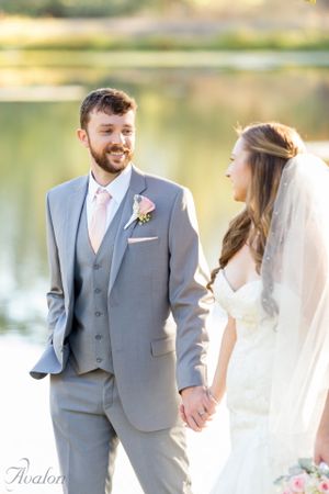 A wedding couple shares a tender moment by a peaceful lake in the afternoon sunlight.