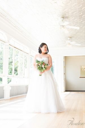 A bride in a classic white ball gown poses in a bright sunlit room with floral bouquet.