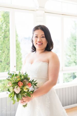 A bride holds a colorful bouquet while posing in a bright white sunroom.