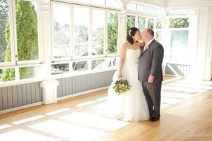 A wedding couple shares an intimate moment in a sunlit room with large windows.