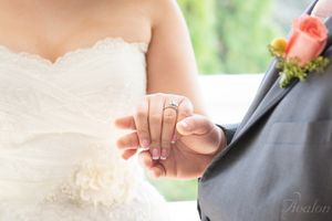 A close-up of newlyweds holding hands showing wedding rings and boutonniere details.