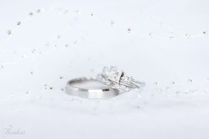 Sparkling diamond engagement ring and wedding band on white textured background.