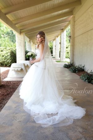 Bride in flowing white gown poses under covered walkway with columns.