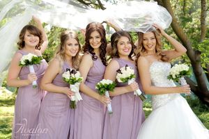 Bridal party in lavender dresses poses with white bouquets outdoors.