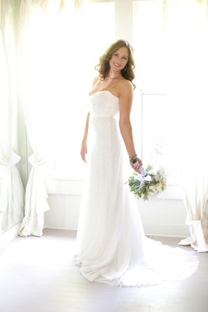 Elegant white strapless wedding gown with flowing train and bridal bouquet in bright natural lighting.