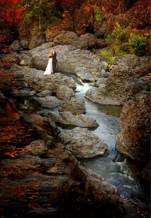 Wedding photo at rocky stream with autumn foliage and cascading water.