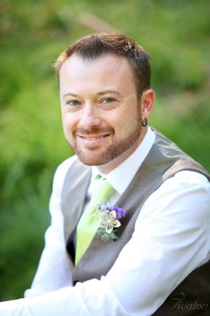 Groom wearing grey vest and lime green tie smiles outdoors in natural setting.