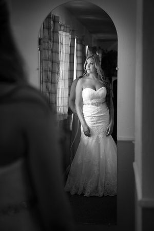 Dramatic black and white bridal portrait through doorway showing fitted lace wedding gown.