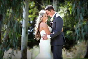 Romantic wedding portrait of couple embracing under willow trees in soft natural light.