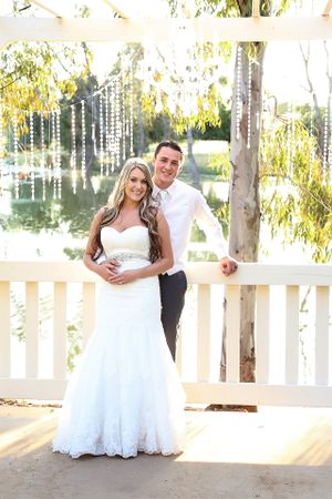Wedding couple posing on white deck with hanging crystal decorations and lake backdrop.