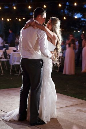 First dance moment at outdoor wedding reception under string lights at dusk.